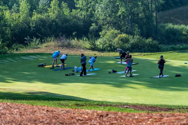 A group practicing yoga together on a golf course fairway in the morning