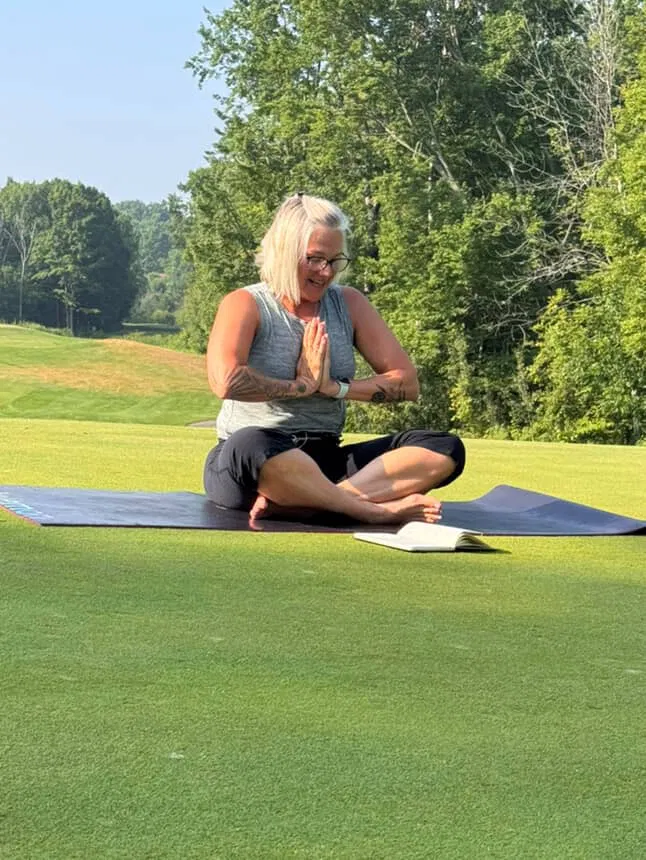 Smiling student in a seated prayer pose on a golf course