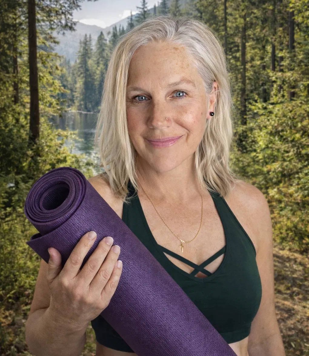 Stacey J, founder and lead instructor of Every Branch, holding a rolled yoga mat in a forest
